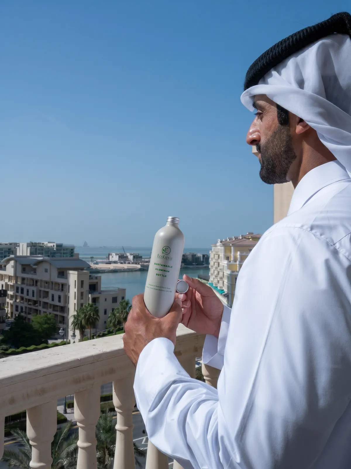 A man on a balcony holding an EcoLuxia aluminum bottle, with the marina behind him.