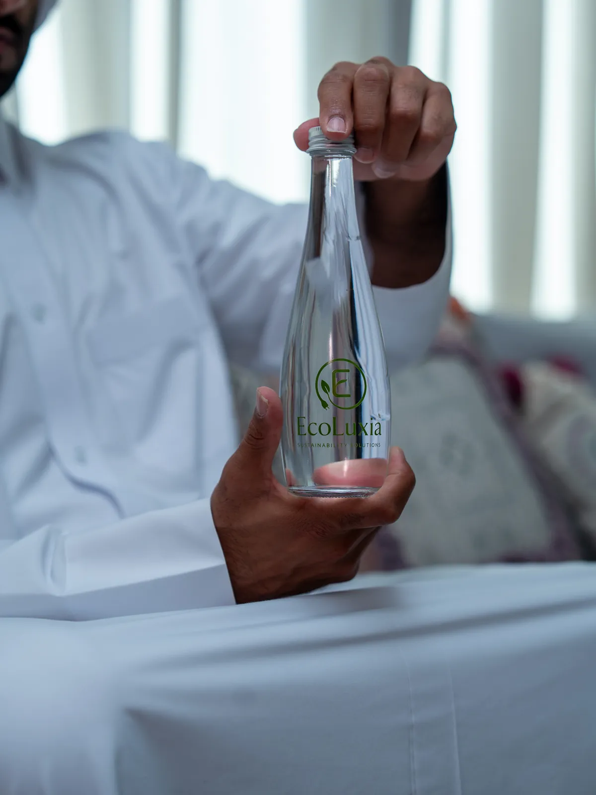 Hands holding an EcoLuxia glass bottle by its neck.