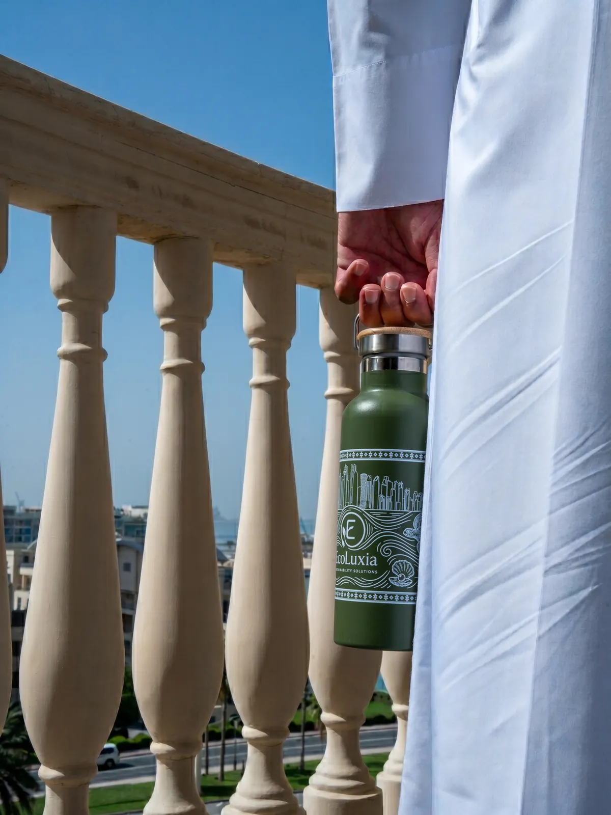 An EcoLuxia stainless-steel bottle held beside the balusters of a balcony.