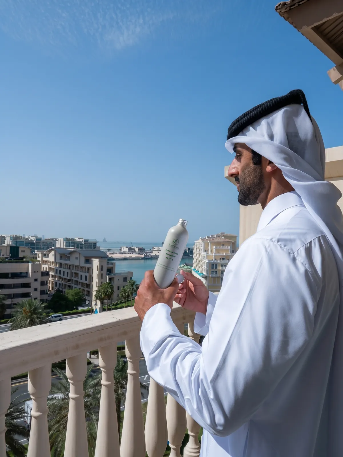 A man on a balcony looking out over the waterfront, an EcoLuxia aluminum bottle in his hand.